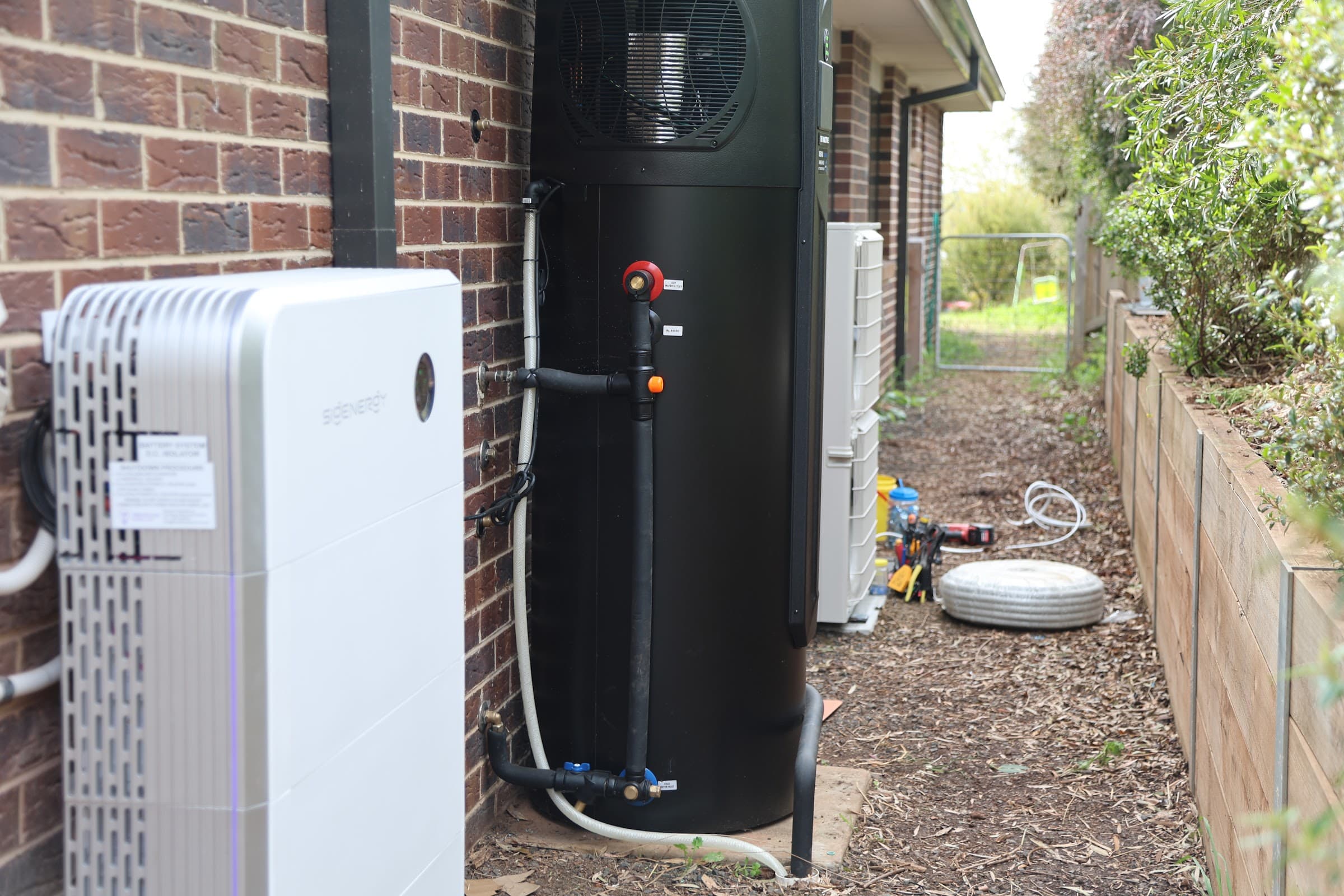 Heat-pump hot water and battery installed along the side of a house