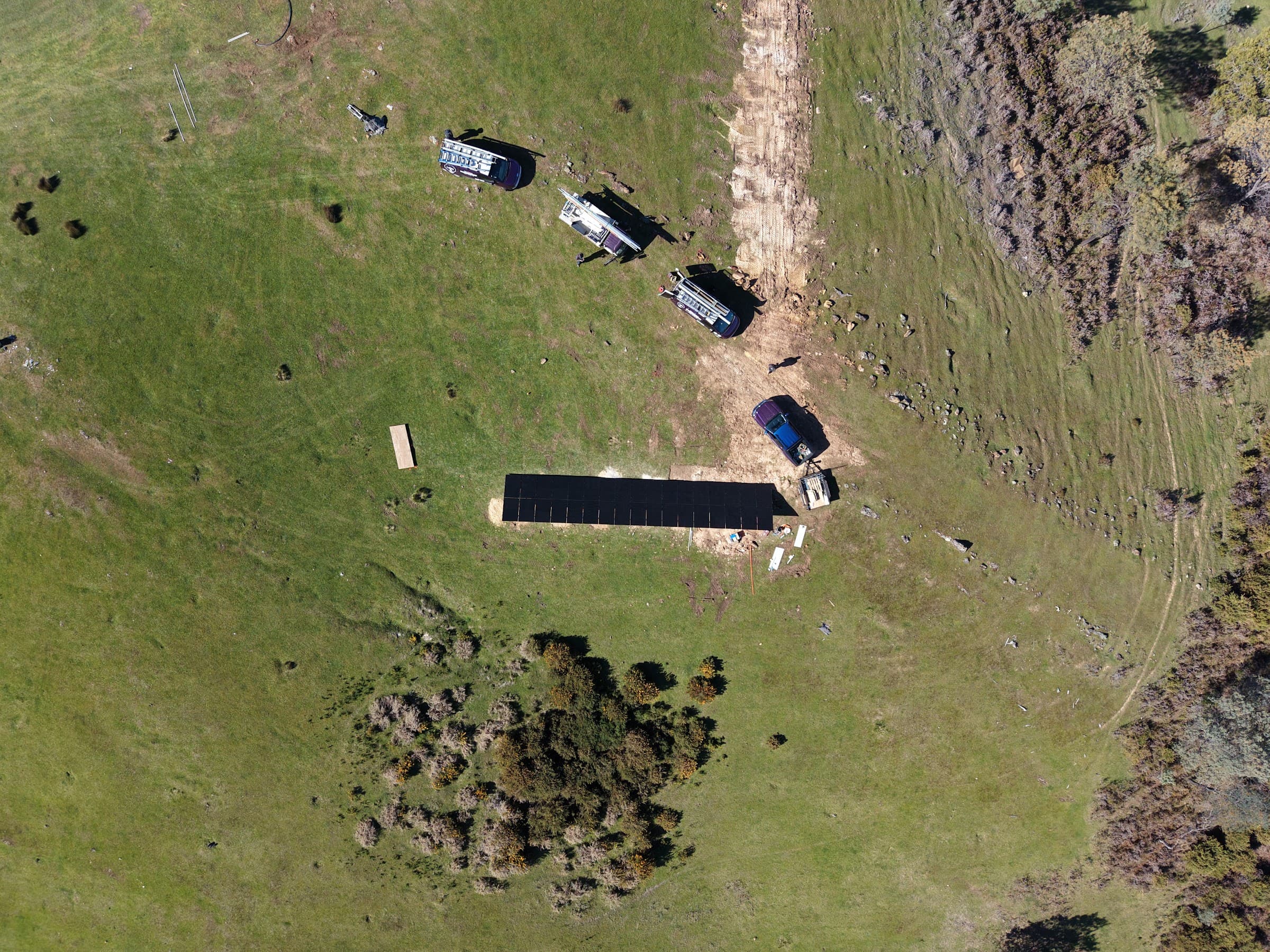 Top-down aerial of the ground-mount array and work vehicles on an isolated hillside
